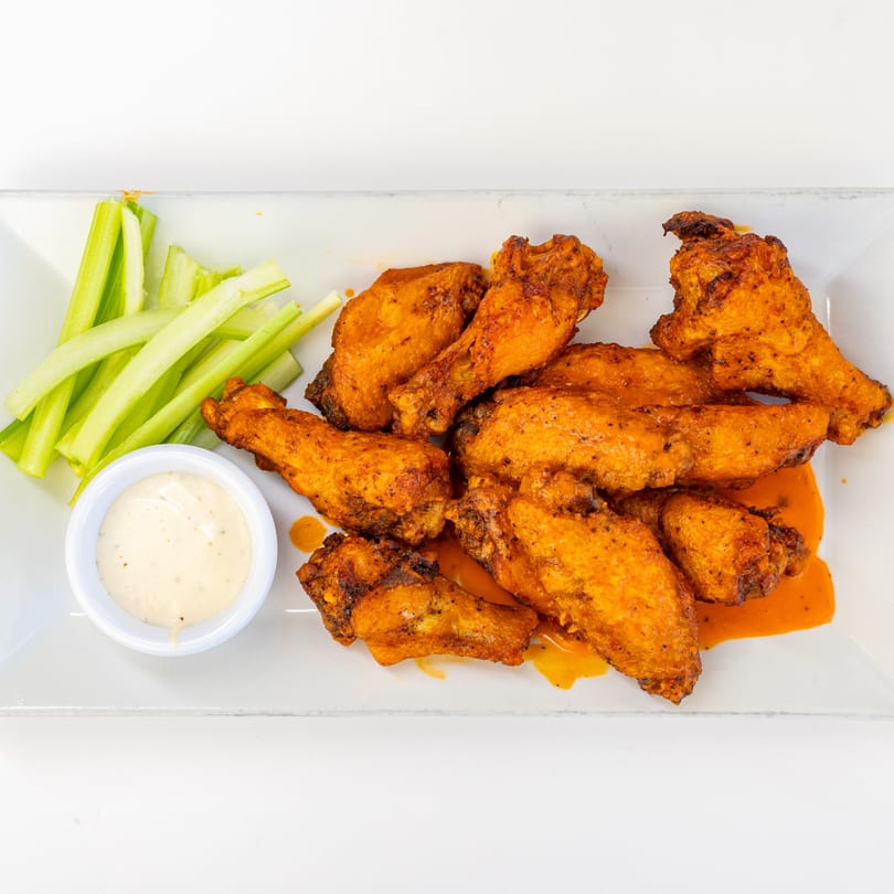 A plate of Brother's Pizza Radio Hill's buffalo wings with celery sticks and ranch dressing.