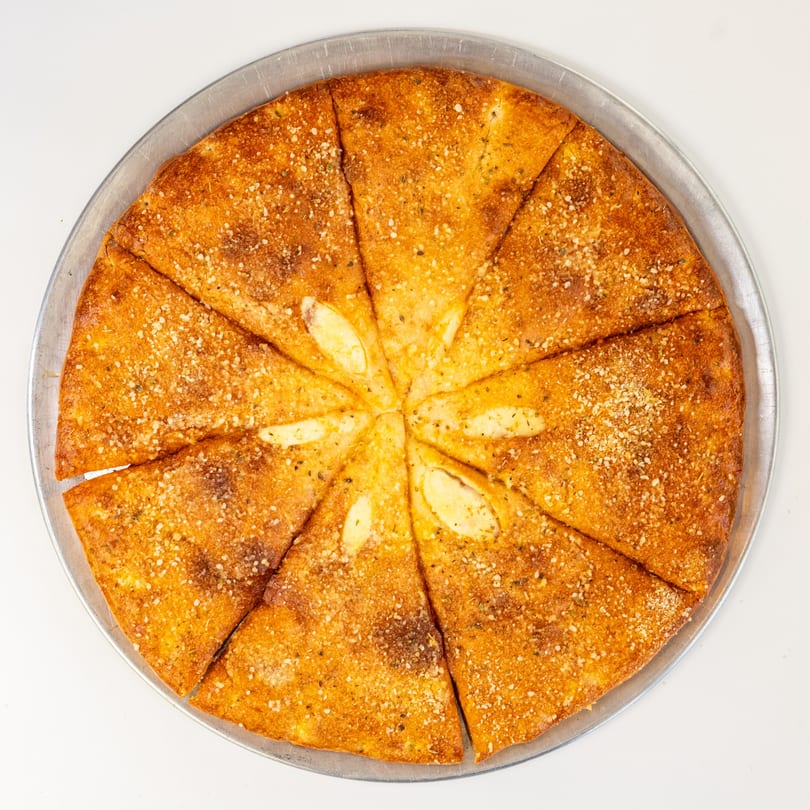 A golden-brown garlic knot pizza, cut into slices, on a metal pizza pan.