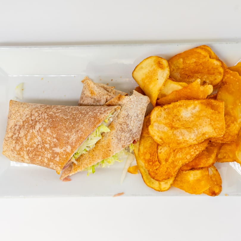 A whole wheat wrap filled with lettuce and meat, served with a side of potato chips.